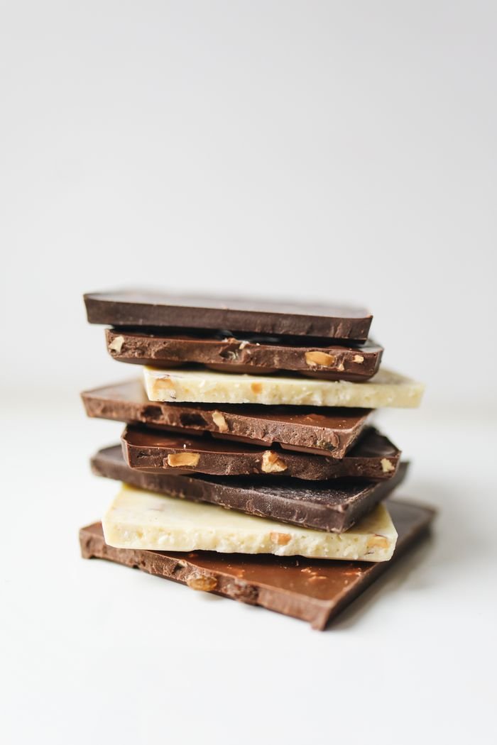 Assorted stacked chocolate bars featuring white, milk, and dark varieties with nut inclusions.